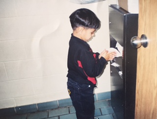 A young boy standing at a door, copying a hand action.