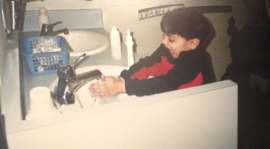 Qasim smiling as he washes his hands at a bathroom sink.