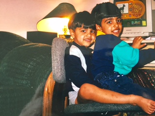 Two boys sitting close together in an armchair at a computer, smiling.