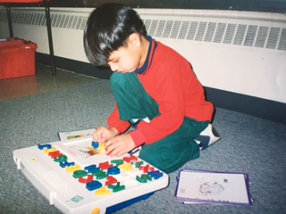 Qasim sitting on the floor working on a colourful letter and shape board.