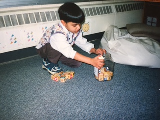 Qasim crouching on the floor beside wooden blocks and a jar.