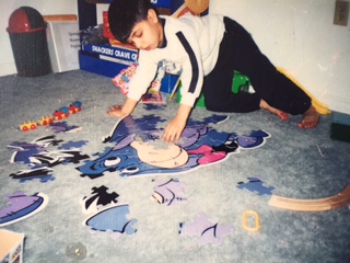 Qasim reaching across a large floor puzzle to place a piece.